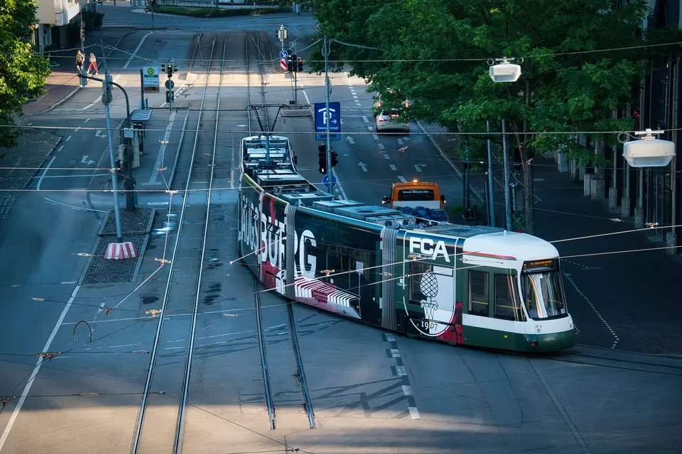 Eine Straßenbahn gleitet durch die urbanen Straßen von Augsburg, Deutschland, umgeben von Bäumen und Verkehr.