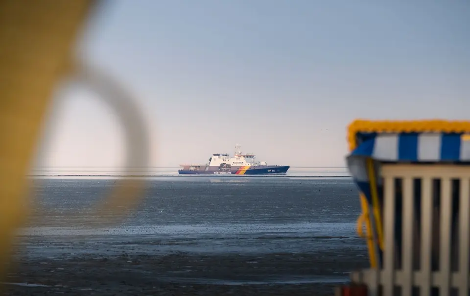Ein Schiff fährt auf der Nordsee in der Nähe von Cuxhaven, Deutschland, mit Strandkörben im Vordergrund.