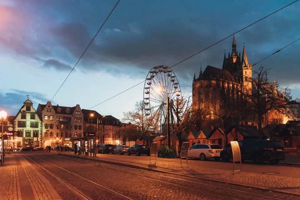 Abendansicht von Erfurt, Deutschland, mit einem Riesenrad und Kathedrale vor einem lebhaften Himmel.