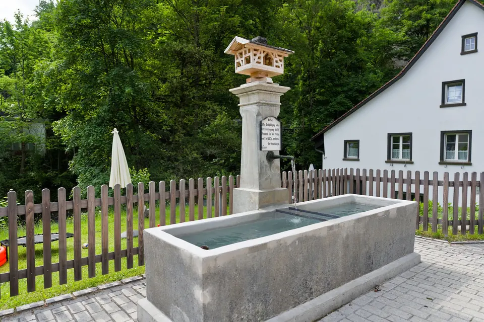 Uriger Steintrog mit rustikalem Vogelhaus aus Holz in idyllischer Schweizer Landschaft.