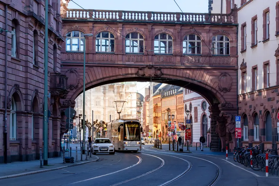 Eine Straßenbahn fährt an einem sonnigen Tag in Frankfurt unter einem historischen Torbogen hindurch.