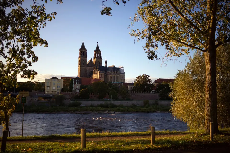 Malersiche Ansicht der Magdeburger Kathedrale und der Elbe bei Sonnenuntergang, die städtische Schönheit hervorhebend.