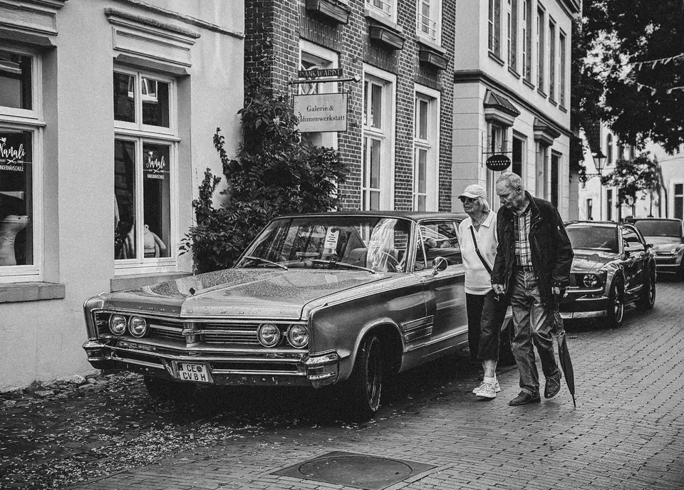 Ein Oldtimer parkt auf einer Kopfsteinpflasterstraße in Leer, Deutschland; ein älteres Ehepaar geht vorbei.