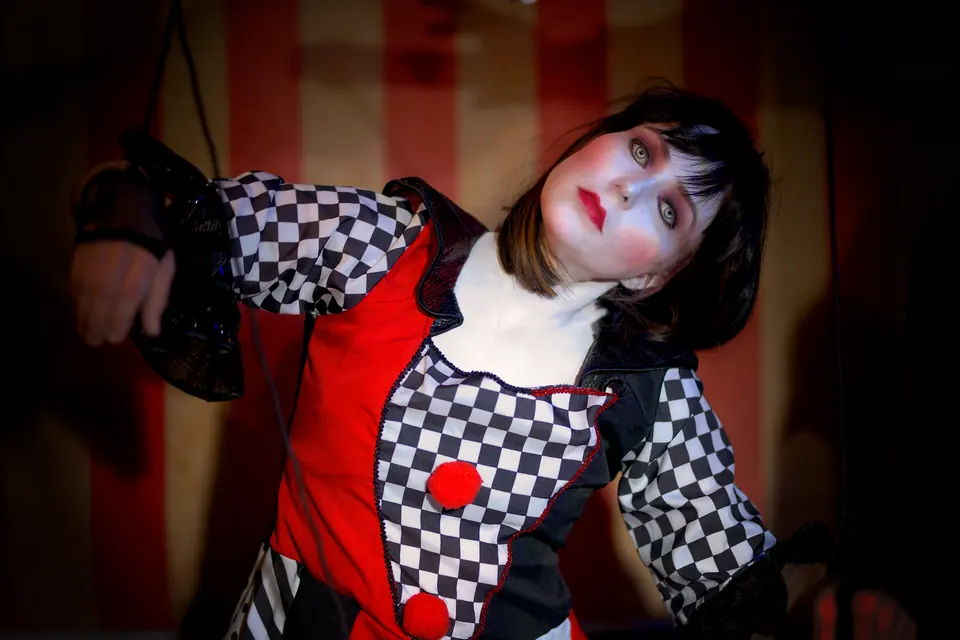 Ein Harlekin-Marionettenkostüm mit dramatischem Make-up, das an ein Theater- oder Halloween-Thema erinnert.