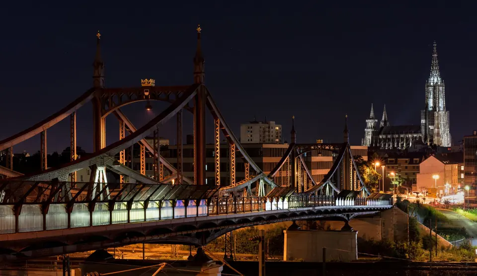 Wunderschön beleuchtete Brücke und Stadtansicht mit einer Kathedrale bei Nacht, die die Stadtarchitektur zeigt.